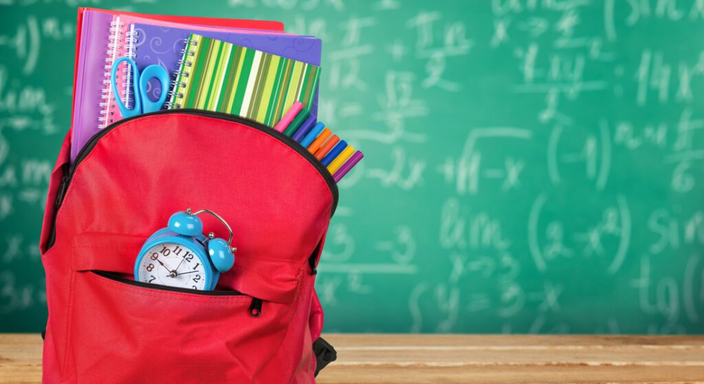 Backpack with books and school supplies in front of a chalkboard