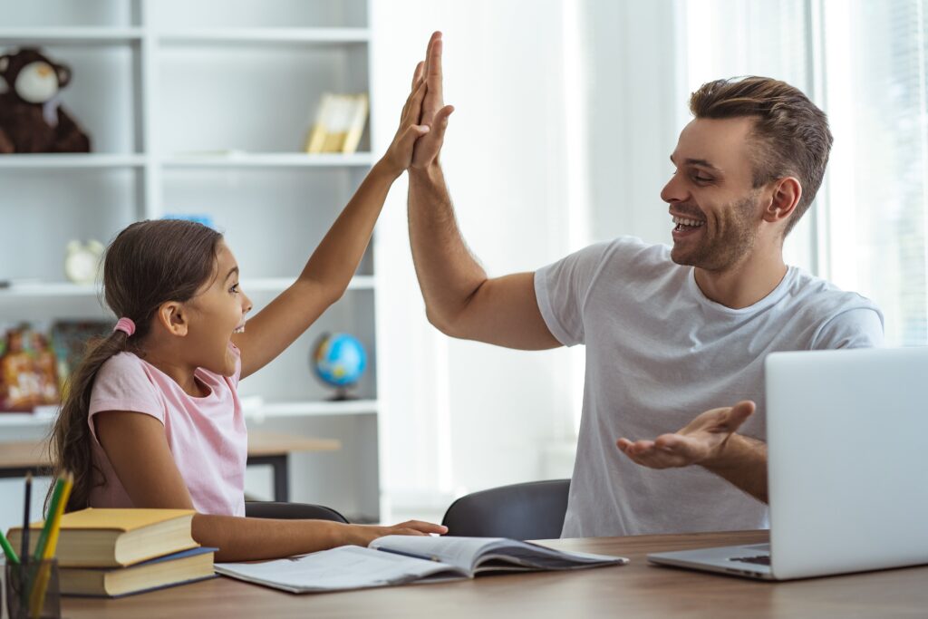 Father and young daughter high-fiving while completing homework.
